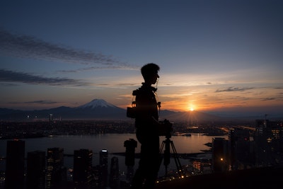 二子玉ビルの屋上から富士山のシルエットを撮影するためカメラをセット。都市の無機質な風景に胸が痛み、温かみや自然の生命力を感じる場所を再発見したいと思ったモバイルアイテムまみれのカメラマンのシルエット